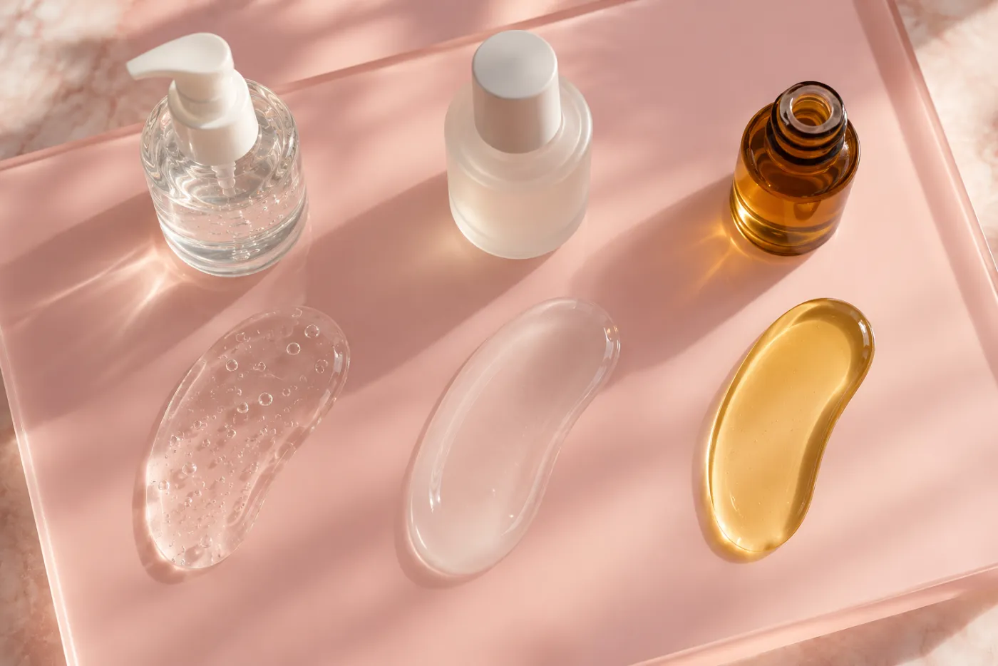 Water-based vs silicone lube vs oil lube swatches side by side on a pink board